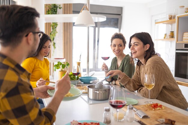 Group of friends eating pasta together in the kitchen