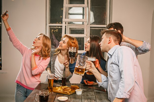 Группа друзей, наслаждаясь вечерними напитками с пивом на деревянный стол