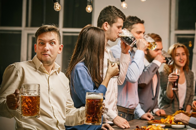 Группа друзей, наслаждаясь вечерними напитками с пивом на деревянном столе
