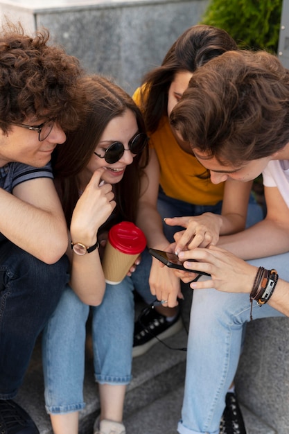 Gruppo di amici che bevono caffè all'aperto in città e guardano lo smartphone