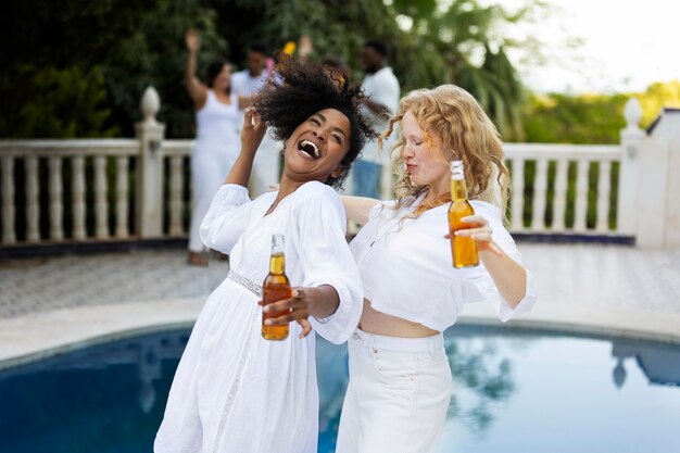 Group of friends having fun during a white party with drinks by the pool