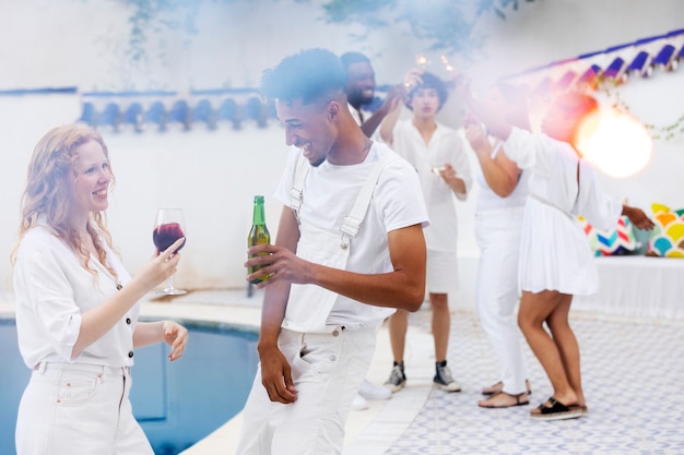 Group of friends having fun during a white party with drinks by the pool