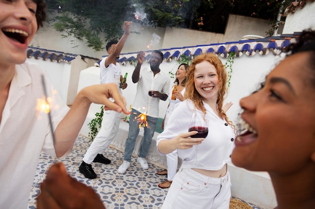 Group of friends having fun with sparklers and drinks at a white party