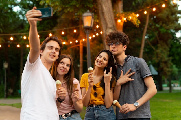 Группа друзей, имеющих мороженое на открытом воздухе и делающих селфи