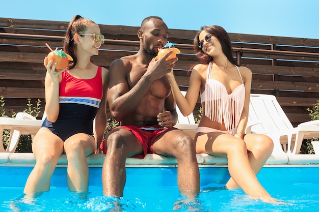 Group of friends playing and relaxing in a swimming pool during summer holidays