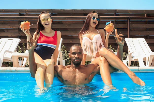 Group of friends playing and relaxing in a swimming pool during summer holidays