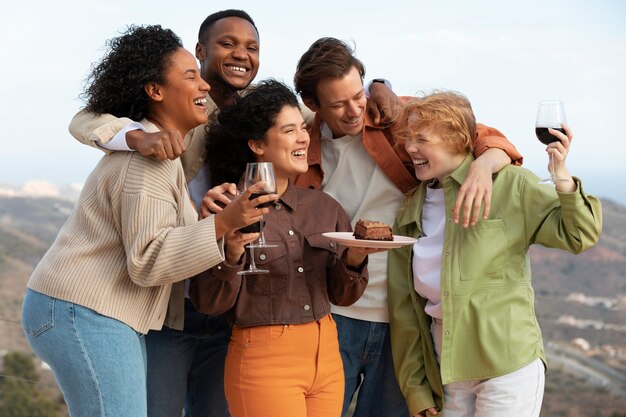 Group of friends posing with glasses of wine and cake during outdoor party