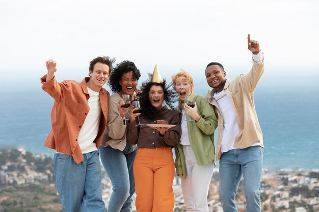 Group of friends posing with glasses of wine and cake during outdoor party