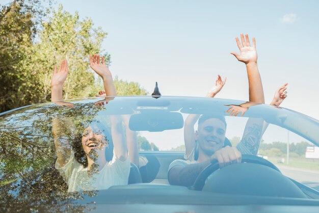 Group of friends raising arms in car