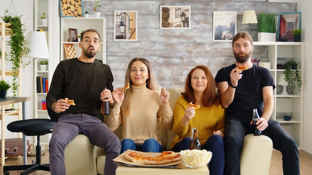 Group of friends relaxing together in living room playing video games using wireless controllers.