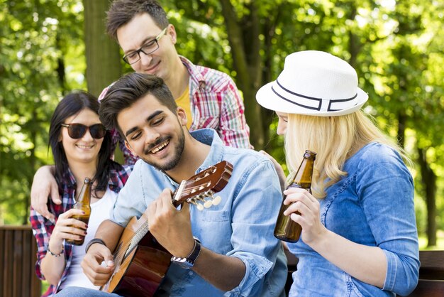 Group of friends sitting on a bench playing guitar and enjoying their time