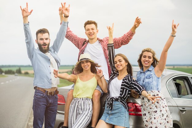 Group of friends standing in front of car raising hands gesturing