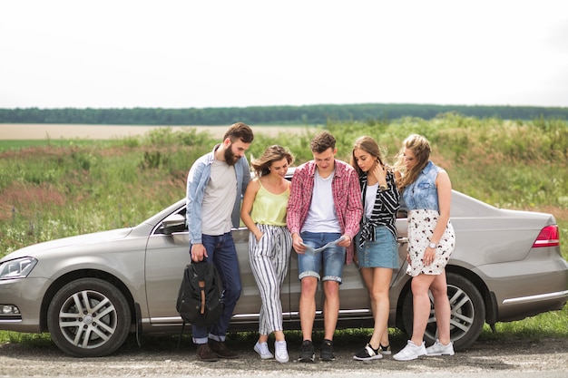 Группа друзей, стоящих рядом с автомобилем, глядя на карту на обочине дороги