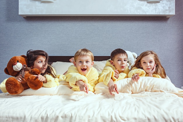 group of friends taking good time on bed. Happy laughing kids, boys and girls playing on white bed in bedroom.
