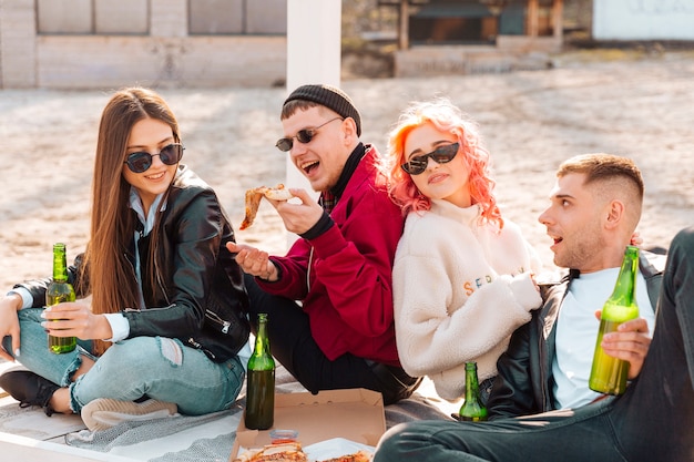 Group of friends with beer and pizza having fun sitting outdoors