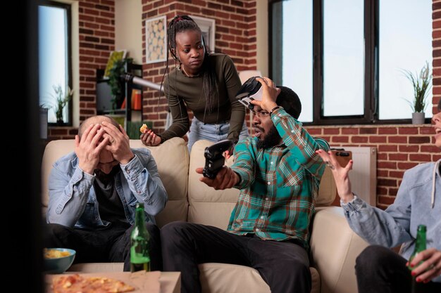 Group of frustrated friends losing video games play with vr glasses and console, drinking bottles of beer. Friends feeling sad about lost gameplay competition, having fun together at gathering.
