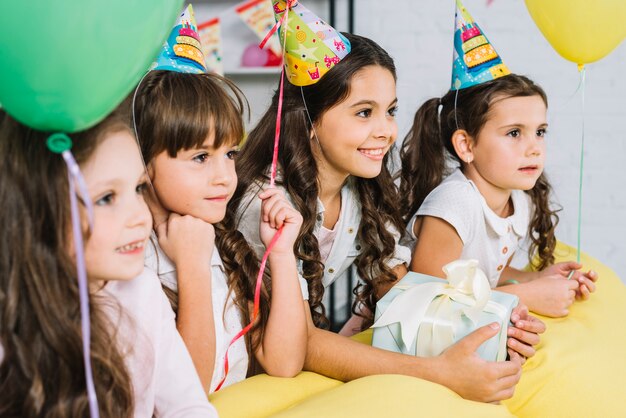 Group of girls wearing party hats and balloons looking away