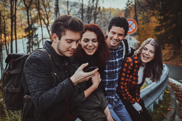 Group of good friends have fun while sitting on the side road at autumn forest.