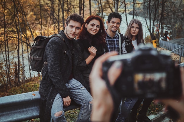 Group of good friends have fun while sitting on the side road at autumn forest.