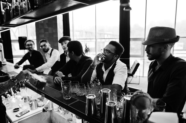 Группа красивых ретро хорошо одетых мужчин-гангстеров проводит время в клубе, пьет виски за барной стойкой Многоэтнический мужской мальчишник мафиозная вечеринка в ресторане