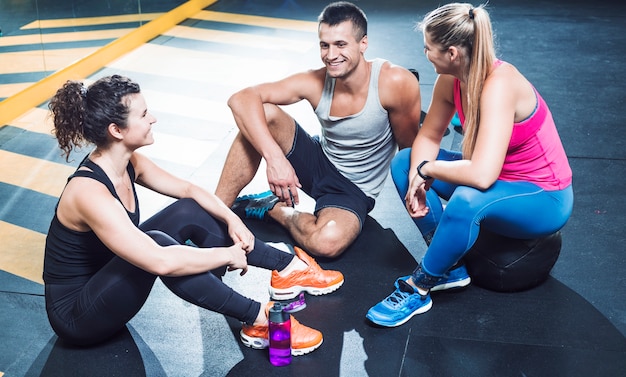 Group of happy athletic people sitting on floor after workout in health club