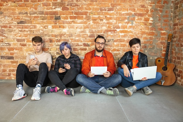 Group of happy caucasian young people sitting behind the brick wall.
