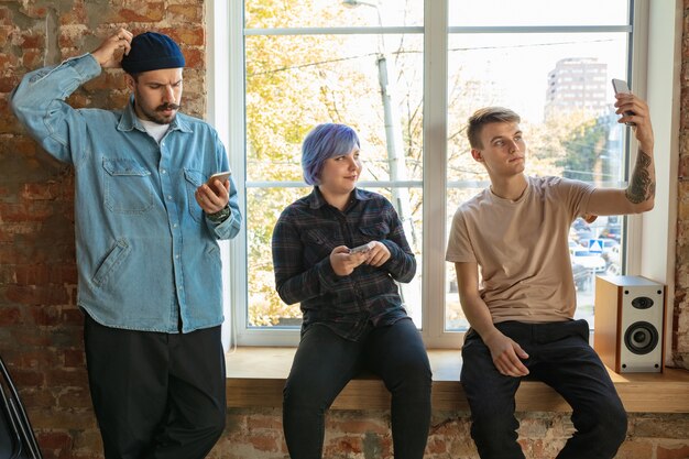 Group of happy caucasian young people standing behind the window. Sharing a news, photos or videos from smartphones, making selfie or playing games and having fun. Social media, modern technologies.