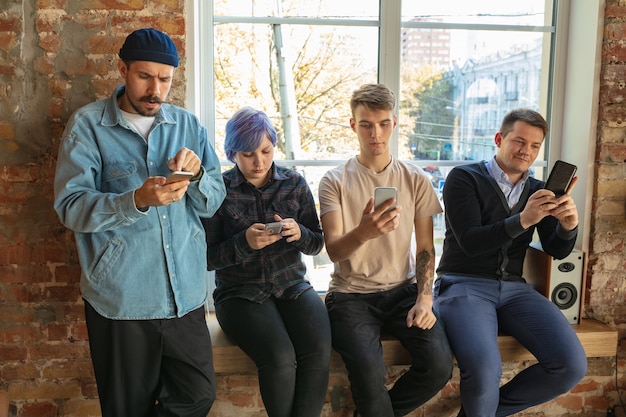 Group of happy caucasian young people standing behind the window. sharing a news, photos or videos from smartphones, talking or playing games and having fun. social media, modern technologies.