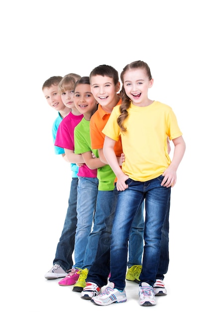 Group of happy children in colorful t-shirts stand behind each other on white wall.