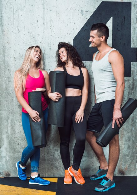 Group of happy fit people leaning on wall in gym