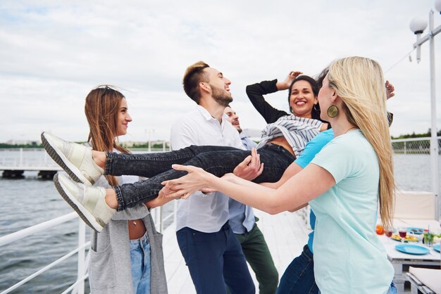 Group of happy friends at the beach, man tossing a happy woman.