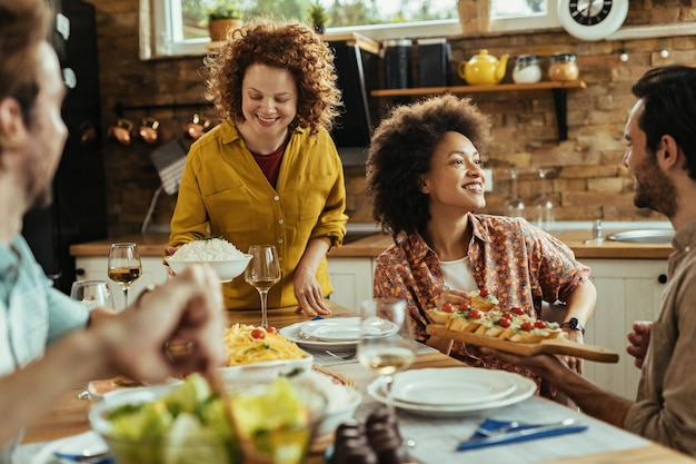 Group of happy friends enjoying conversation and appetizer at dining table at home.