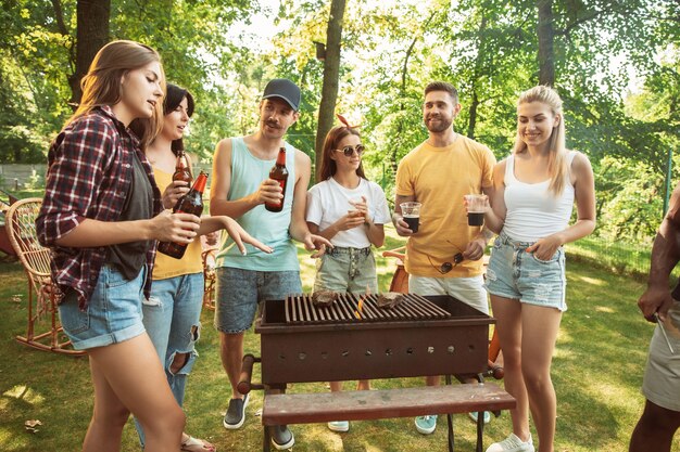 Free photo group of happy friends having beer and barbecue party at sunny day. resting together outdoor in a forest glade or backyard. celebrating and relaxing, laughting. summer lifestyle, friendship concept.