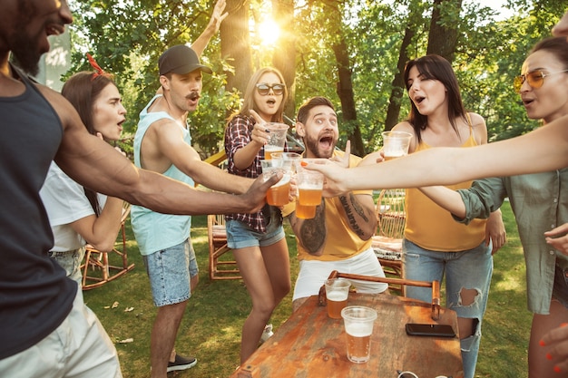 晴れた日にビールとバーベキューパーティーをしている幸せな友人のグループ。森の空き地や裏庭で屋外で一緒に休む