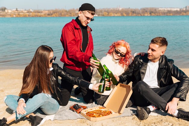 Group of happy friends having fun and clinking bottles on beach