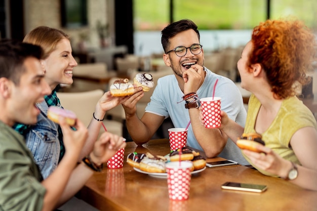 Free photo group of happy friends having fun while eating donuts in a cafe