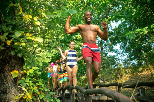 Group of happy friends having fun while running to swim on river.