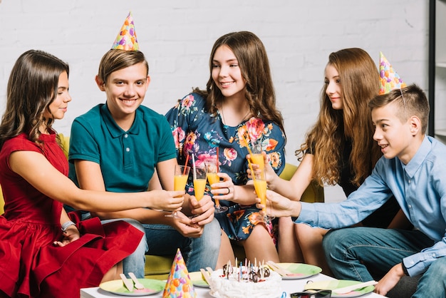Группа счастливых друзей, глядя на день рождения мальчика, держащего стакана сока в партии