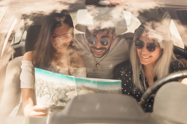Группа счастливых друзей, глядя на карту, сидя внутри автомобиля