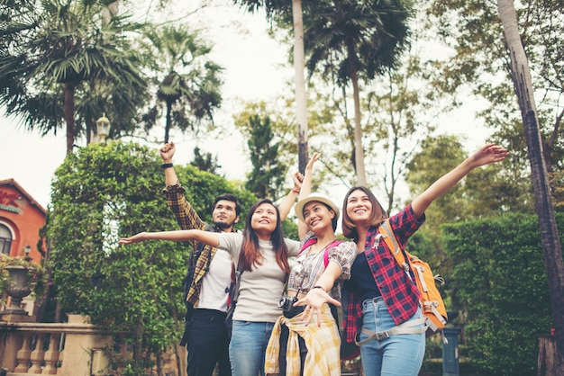 Group of happy friends raised hands on background of city. 