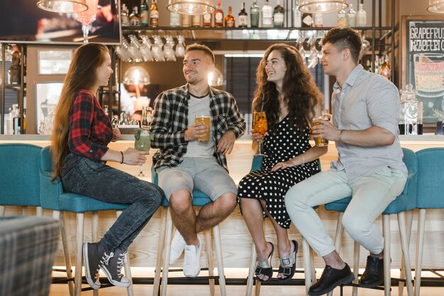 Group of happy friends sitting together with drinks at bar counter