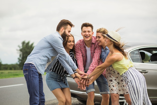 Group of happy friends standing on road putting hands together