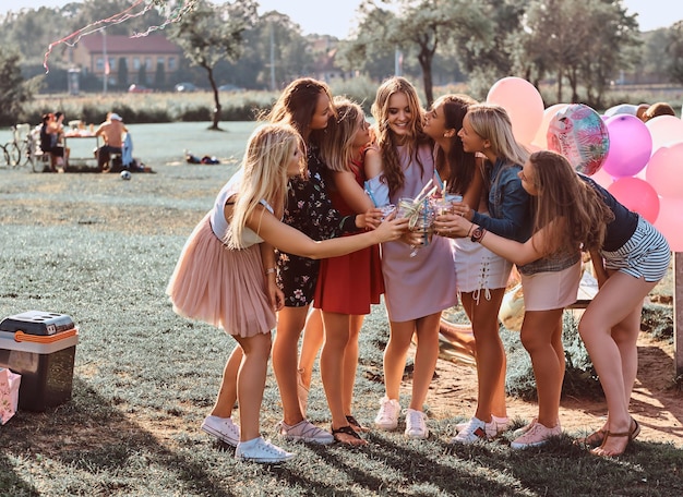 Foto gratuita gruppo di amiche felici divertendosi insieme festeggiando un compleanno al parco all'aperto. amici felici che fanno il tifo con il succo alla festa di picnic all'aperto.