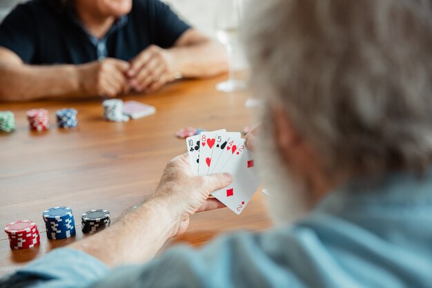 Group of happy mature friends playing cards and drinking wine