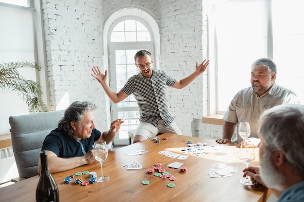 Группа счастливых зрелых друзей, играющих в карты и пьющих вино