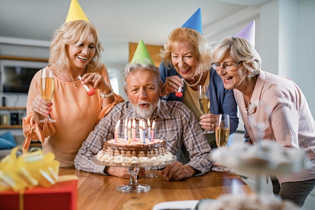 男がケーキにろうそくを吹いている間、誕生日パーティーで楽しんでいる幸せな先輩のグループ