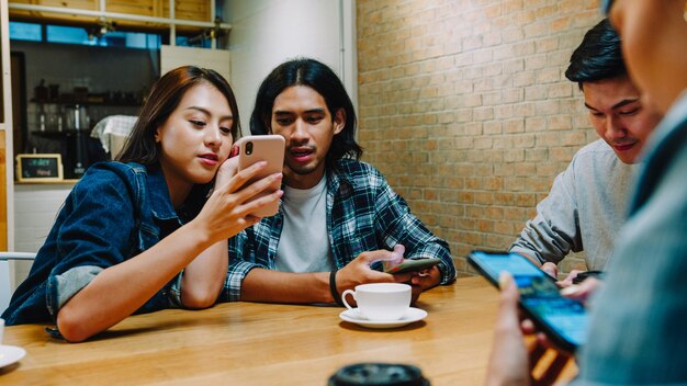 Группа счастливых молодых азиатских друзей, весело проводящих время и используя смартфон вместе, сидя вместе в кафе-ресторане.