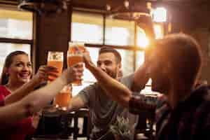 Foto gratuita gruppo di giovani felici che brindano con la birra e si divertono in un pub