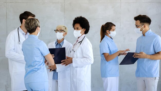 Group of healthcare workers with protective face masks talking at hospital hallway