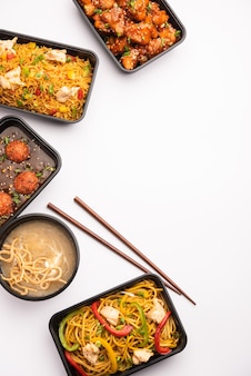 Group of home delivered indo chinese food in plastic packages, containers or boxes containing schezwan noodles, fried rice, chilli chicken, manchurian and soup.